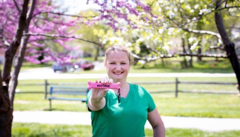 Female owner of company wearing green shirt holding pink bone in front of her in a sunny park